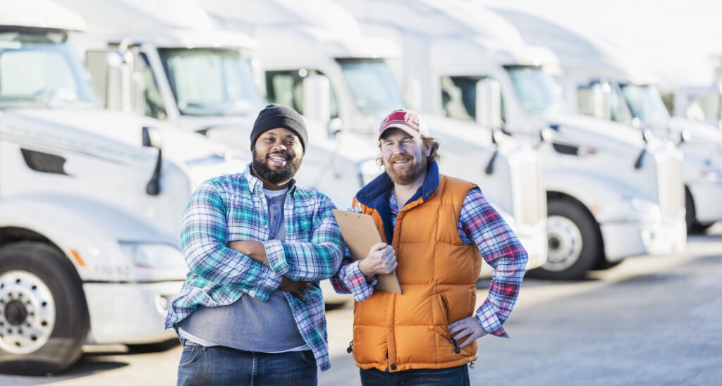 Two men standing in front of a small fleet of trucks